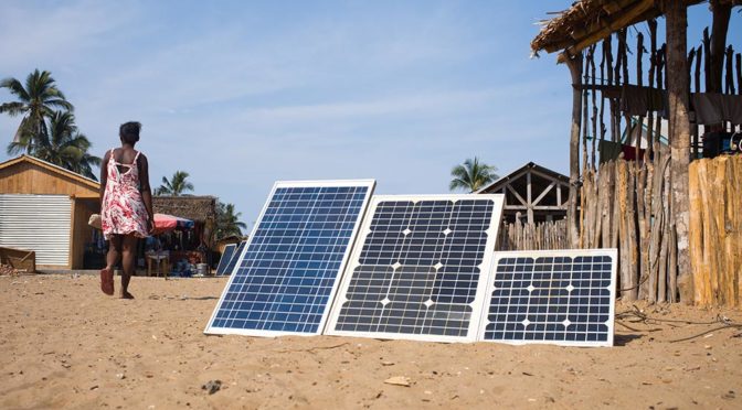 Solar panels in the foreground of African village with woman walking by in the background