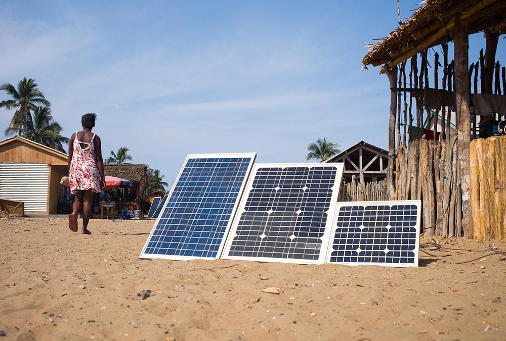 Solar panels in the foreground of African village with woman walking by in the background